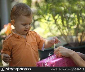 Two years old baby boy helps his mother unpack a gift. Outdoor.