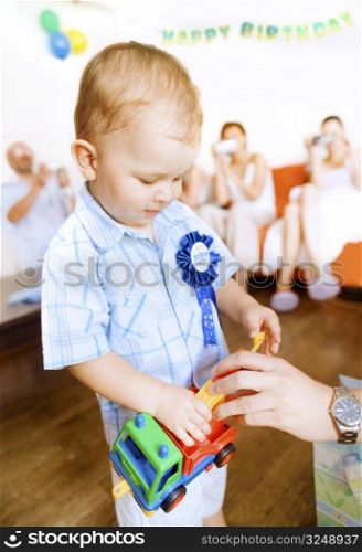 Two years old baby boy on his birthday party with relatives taking shots in the bachground.