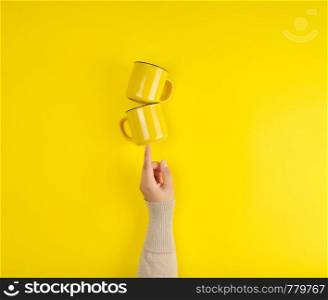 two yellow ceramic cups are supported by a female hand on a yellow background, copy space