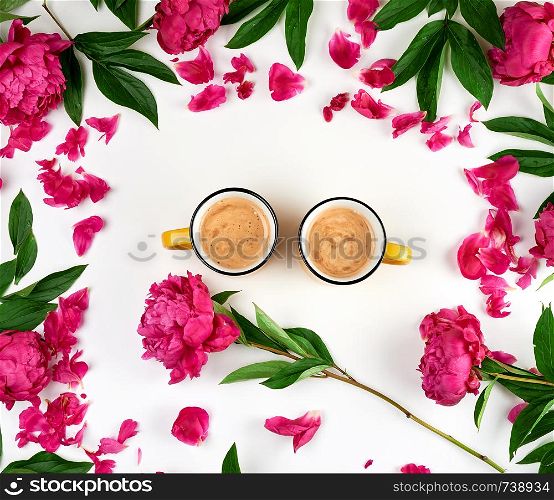 two yellow ceramic cups with black coffee on a white background, next is a bouquet of red peonies with green leaves, top view