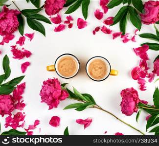 two yellow ceramic cups with black coffee on a white background, next is a bouquet of red peonies with green leaves, top view