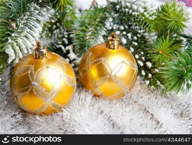 Two yellow New Year&acute;s balls and snow-covered branches of a Christmas tree