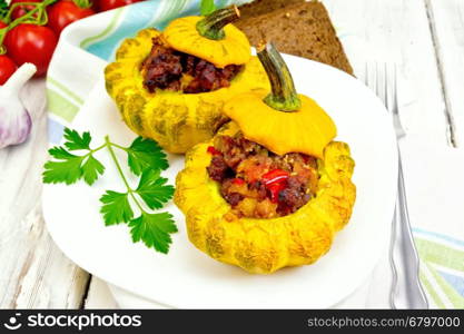 Two yellow squash stuffed with meat, tomatoes and peppers in the dish, bread, garlic, parsley and fork on a wooden board