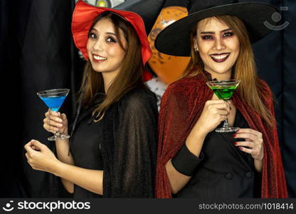 Two young adult and teenager girls celebrating a Halloween party carnival Festival in Halloween costumes drinking alcohol cocktail