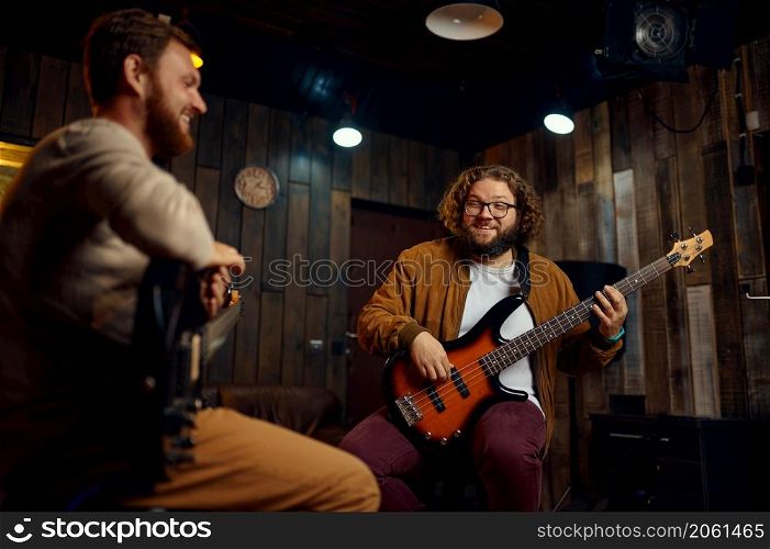 Two young adult male friends playing electric guitars at studio. Improvised rock band. Music lesson. Happy smiling friends musician playing electric guitar