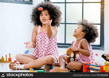 Two young African girls play together that older throw some toys and younger girl look fun with the activity.