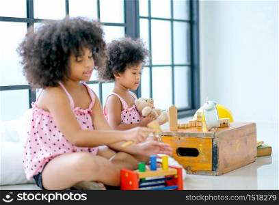 Two young African girls play toys together with main focus on front girl who look enjoy with her toys.
