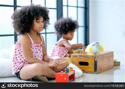 Two young African girls play toys together with main focus on front girl who look boring with her toys but the other look enjoy.