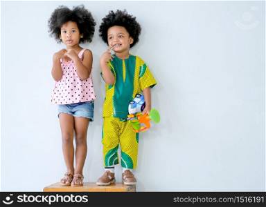 Two young African little boy and girl stand in front of white wall and express different action and they look relax and fun with boy hold some toys in his hand.