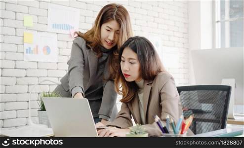 Two young Asian businesswomen working together in office at small business sitting reading a report or paperwork with pleased smiles and successful teamwork. Business, technology and office concept.
