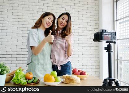 Two young asian woman food bloggers talking and thumb up while recording video, vlog concept, people, food and technology communication