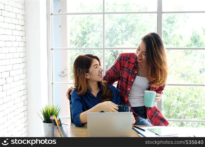 Two young asian women working with laptop computer at home office with happy emotion, working from home, small business, office casual lifestyle concept