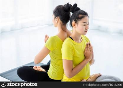 Two young Asian women workout practicing yoga in yellow dress or pose with a trainer and practice meditation wellness lifestyle and health fitness concept in a gym.