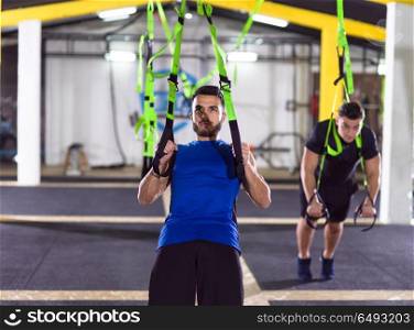 two young athlete men working out pull ups with gymnastic rings at the crossfitness gym. men working out pull ups with gymnastic rings