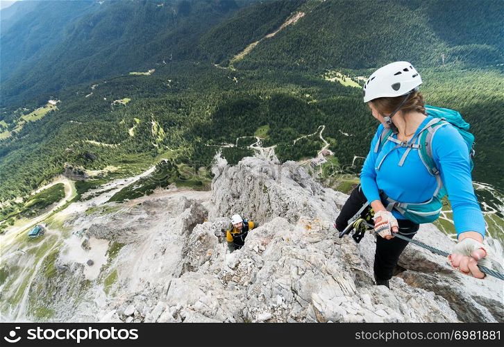 two young attractive mountain climbers on very exposed Via Ferrata in the Dolomites of Italy