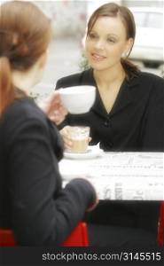 Two young Australian woman sitting at a cafe happy discussing and conversing. Both dressed in corporate business suits, Drinking coffee.