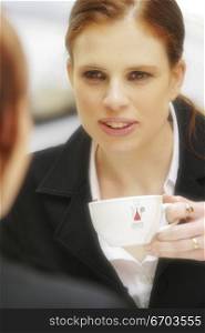 Two young Australian woman sitting at a cafe happy discussing and conversing. Both dressed in corporate business suits, Drinking coffee.