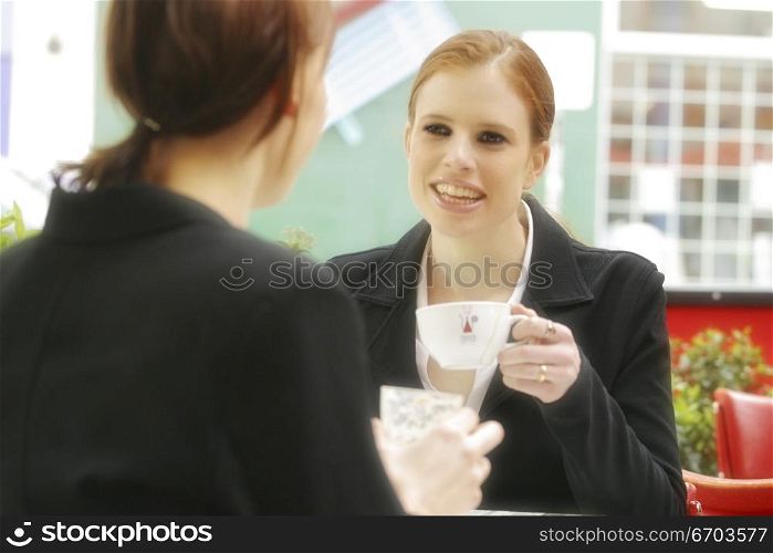 Two young Australian woman sitting at a cafe happy discussing and conversing. Both dressed in corporate business suits, Drinking coffee. Melbourne Australia.
