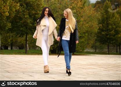 Two Young beautiful women walking in park, on yellow background autumn nature