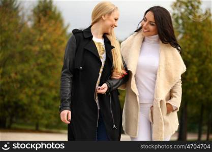 Two Young beautiful women walking in park, on yellow background autumn nature