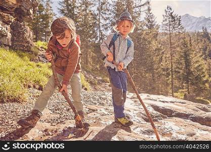 Two young boys, holding sticks, exploring forest