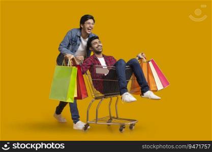 Two young boys laughing with one of them sitting in a trolley holding carrybags.