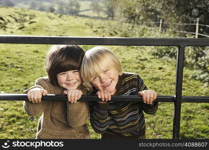 Two young boys on gate in countryside