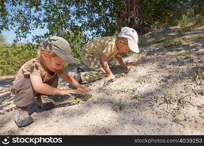 Two young boys, playing with toy cars on sand