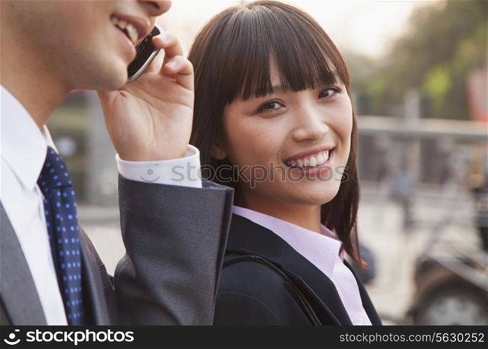 Two young business people outside on the street using phone in Beijing, portrait