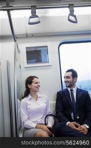 Two young business people sitting and chatting on the subway