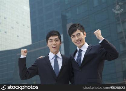 Two young businessmen outside glass building, smiling, portrait