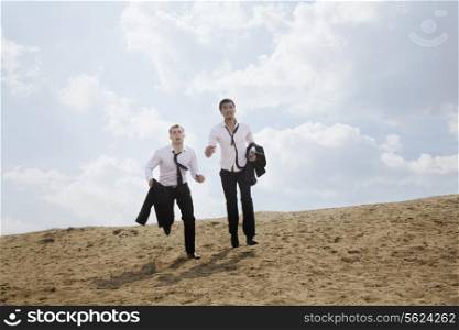 Two young businessmen running and exhausted in the desert, holding jackets