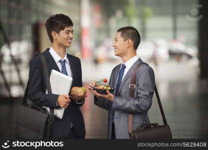 Two young businessmen talking and having a lunch outdoor