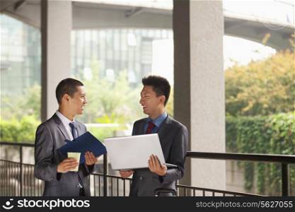 Two young businessmen working outdoor, looking at each other