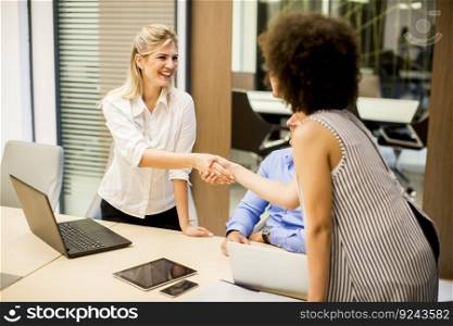 Two young businesswomen shaking hands after a job well done in modern office