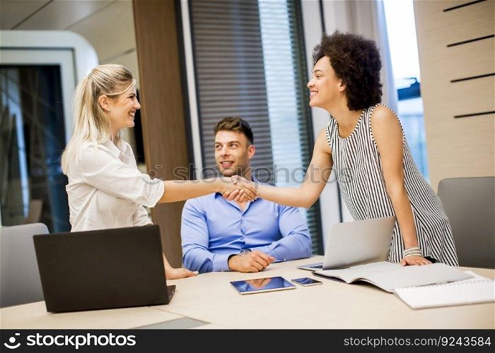 Two young businesswomen shaking hands after a job well done in modern office