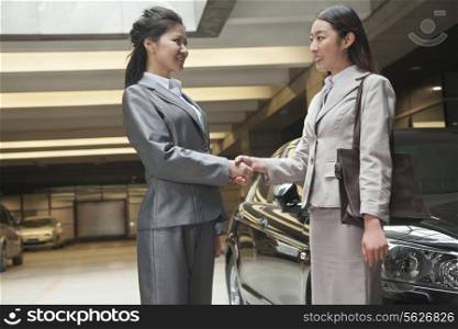 Two young businesswomen shaking hands in parking garage