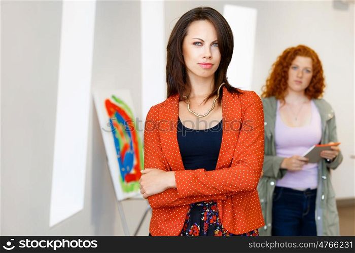 Two young caucasian women standing in art gallery front of paintings. Two young caucasian women standing in an art gallery in front of painting displayed on white wall