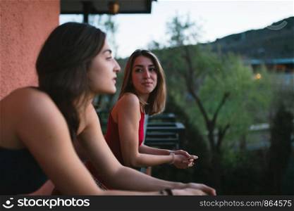 Two young caucasian women watch the sunset from their balcony.