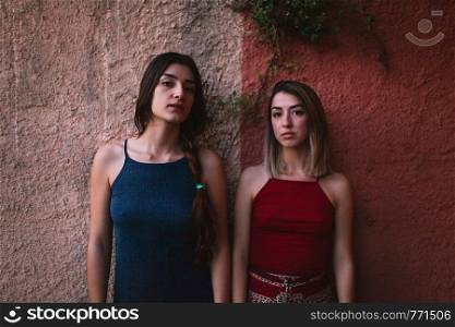 Two young caucasian women watch the sunset from two colors wall