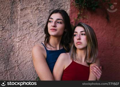 Two young caucasian women watch the sunset from two colors wall