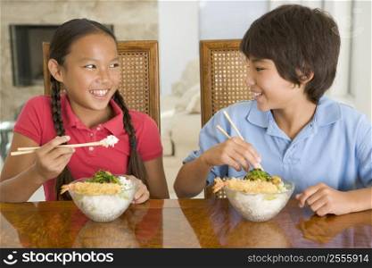 Two young children eating Chinese food in dining room smiling