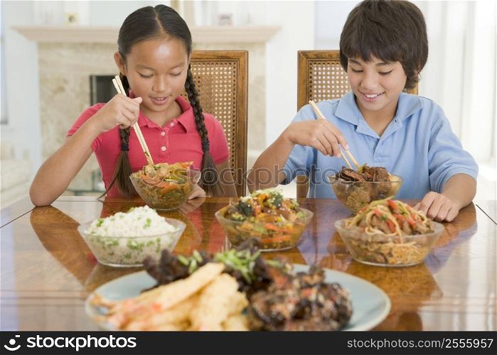 Two young children eating chinese food in dining room smiling