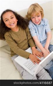 Two young children having fun on a laptop while sitting on a settee