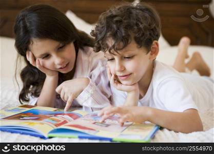 Two young children in bedroom reading book (selective focus)