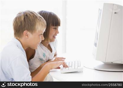 Two young children in home office with computer smiling