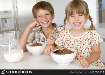Two young children in kitchen eating cereal smiling