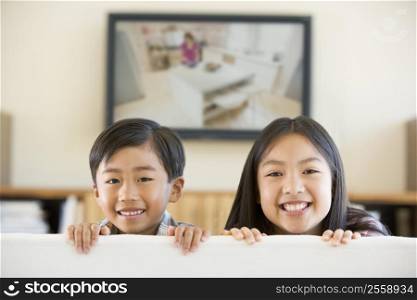 Two young children in living room with flat screen television smiling