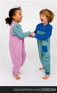 Two young children, one a mixed race little girl the other a blonde boy, holding hands and bouncing around having fun