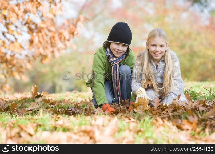 Two young children outdoors at park playing in leaves and smiling (selective focus)